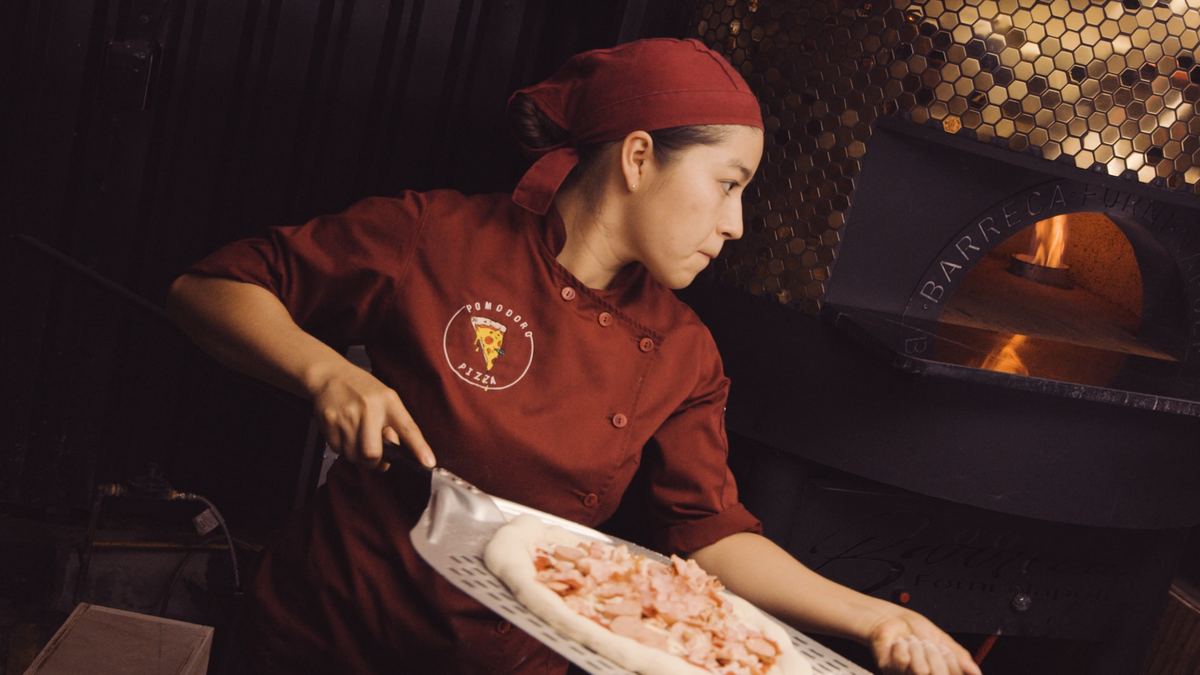 Pizzera de Pomodoro llevando una pizza al horno con la pala